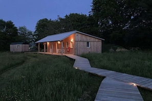 Eine Holzhütte mit Veranda, ein kleines Gartenhaus und ein Holzweg, der zur Hütte führt.