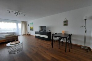 Ein modernes Zimmer mit einer Couch, einem Esstisch mit Stühlen, einem Fernseher und einer Lampe.