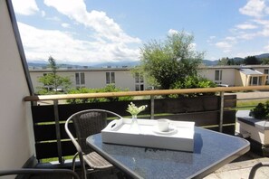 Ein Balkon mit Tisch, Stühlen, einer Ablage mit einer Vase und Tasse sowie Blick auf Gebäude und Bäume.