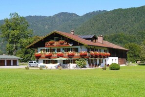Ein zweistöckiges Gebäude mit Balkon, umgeben von einer grünen Wiese und Bergen.
