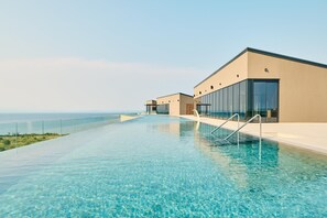 Un hotel moderno con una lunga piscina a sfioro cristallina che si affaccia sull'oceano.