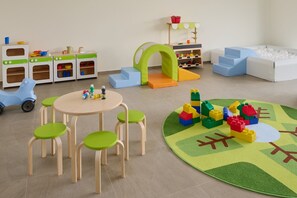 Una sala de juegos con una cocina de juguete, una piscina de bolas y una mesa con sillas.