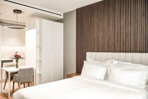 Habitación de hotel moderna con una cama, un escritorio con silla, un jarrón con flores y una pared con listones de madera verticales.