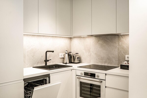 Una cucina moderna con lavastoviglie, doppio lavello, bollitore elettrico, tostapane e forno integrato.