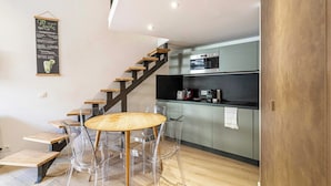 Een moderne keuken met een inbouwoven en koffiezetapparaat, een houten trap en een eethoek met een ronde tafel en transparante stoelen.