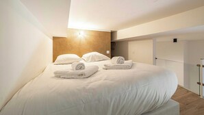 Een moderne hotelkamer met een groot bed, keurig opgevouwen handdoeken, een houten accentmuur en een glazen scheiding.