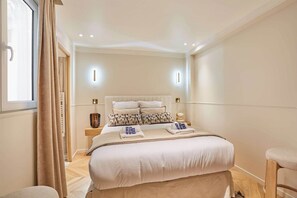 Ein Schlafzimmer mit einem großen Bett, Nachttischen, einem Fenster mit Vorhängen und einem Beistelltisch mit einer Lampe.