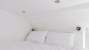 Quarto branco com cama, luminária de teto e arandela na parede.