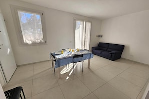 Ein Zimmer mit Esstisch für zwei Personen, einer Couch und zwei Fenstern.