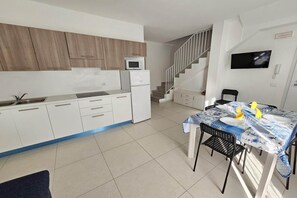 A modern kitchen with white cabinets, a microwave, and a refrigerator. There is a dining area with a table set for two, a chair, and a TV mounted on the wall. - Charming Rosolina Mare Apartment for 6 (Rosolina Mare (RO))