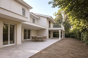 Ein modernes, zweistöckiges Haus mit einem Balkon, einer Terrasse mit Tisch und Stühlen sowie einem Garten.