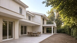 Une maison moderne à deux étages, dotée d’un balcon, d’une terrasse avec une table et des chaises, et d’un jardin.