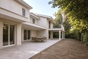 Ein modernes, zweistöckiges Haus mit einem Balkon, einer Terrasse mit Tisch und Stühlen sowie einem Garten.