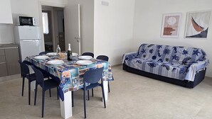 Un coin repas avec une table dressée pour deux personnes, un canapé et un réfrigérateur.