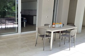 Ein Essbereich mit Tisch und Stühlen, eine Küche im Hintergrund und Blick durch eine Glastür.