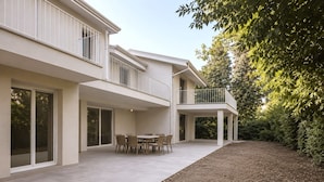 Una casa moderna de dos pisos con un balcón, un patio con mesa y sillas, y un jardín.