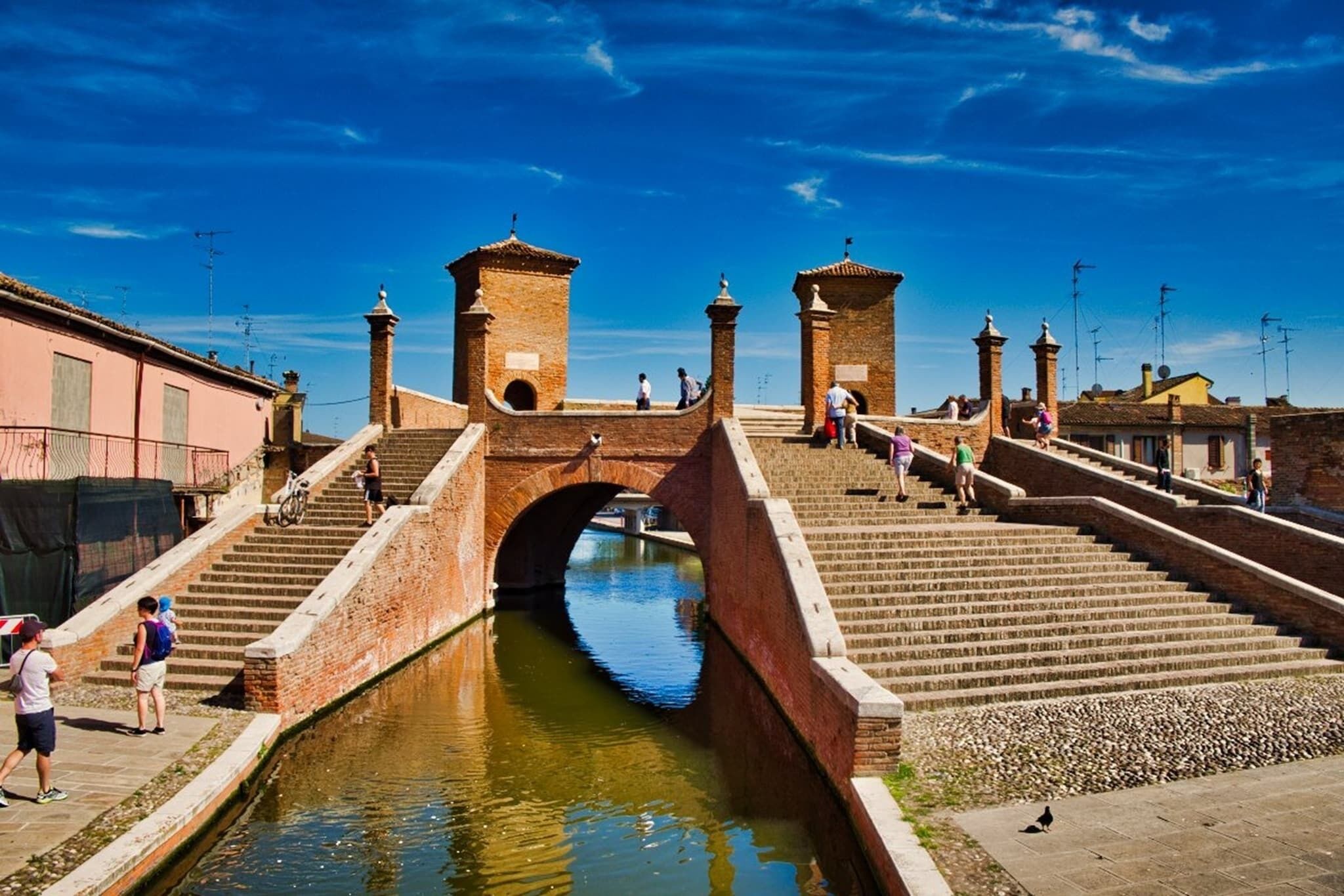 A historic bridge with a canal underneath, stone steps, and a clear blue sky.