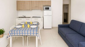 Un espacio habitable compacto con una mesa de comedor lista para cuatro personas, una kitchenette con microondas, refrigerador y un sofá azul.