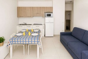 A compact living space with a dining table set for four, a kitchenette with a microwave, a refrigerator, and a blue sofa. - Modern Getaway in Rosolina Mare for 5 (Rosolina Mare (RO))