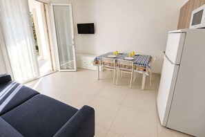 A room with a dining table, chairs, a TV, and a refrigerator. - Modern Getaway in Rosolina Mare for 5 (Rosolina Mare (RO))