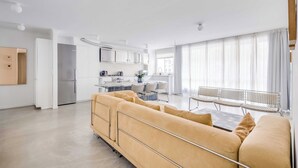 A modern living room with a sofa, a dining table, and a kitchen in the background. - Modern 1BDR/2P flat with a balcony – Ménilmontant (Paris)