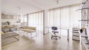 A modern kitchen with white cabinets, a dining area with a glass table, and a workspace with a desk and chair. - Modern 1BDR/2P flat with a balcony – Ménilmontant (Paris)