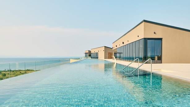 A modern hotel with a long, clear infinity pool overlooking the ocean.