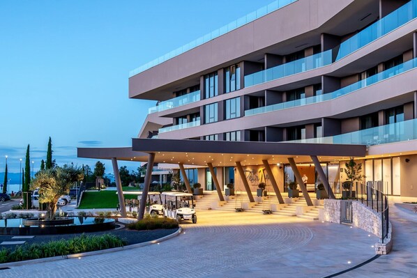 Un hotel moderno con una estructura de varios pisos, un acceso cubierto y un área exterior ajardinada.
