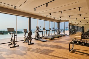 Un gimnasio con máquinas de cardio, pesas y grandes ventanales que ofrecen vistas al exterior.