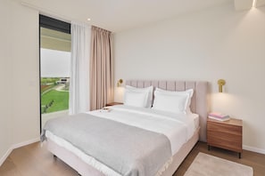 Un dormitorio con una cama grande, una mesita de noche, una lámpara de noche y vistas a un paisaje verde a través de una ventana.