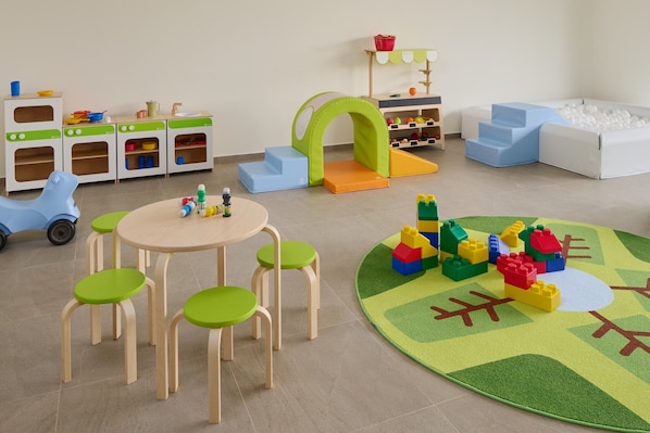Una sala de juegos con una cocina de juguete, una piscina de bolas y una mesa con sillas.