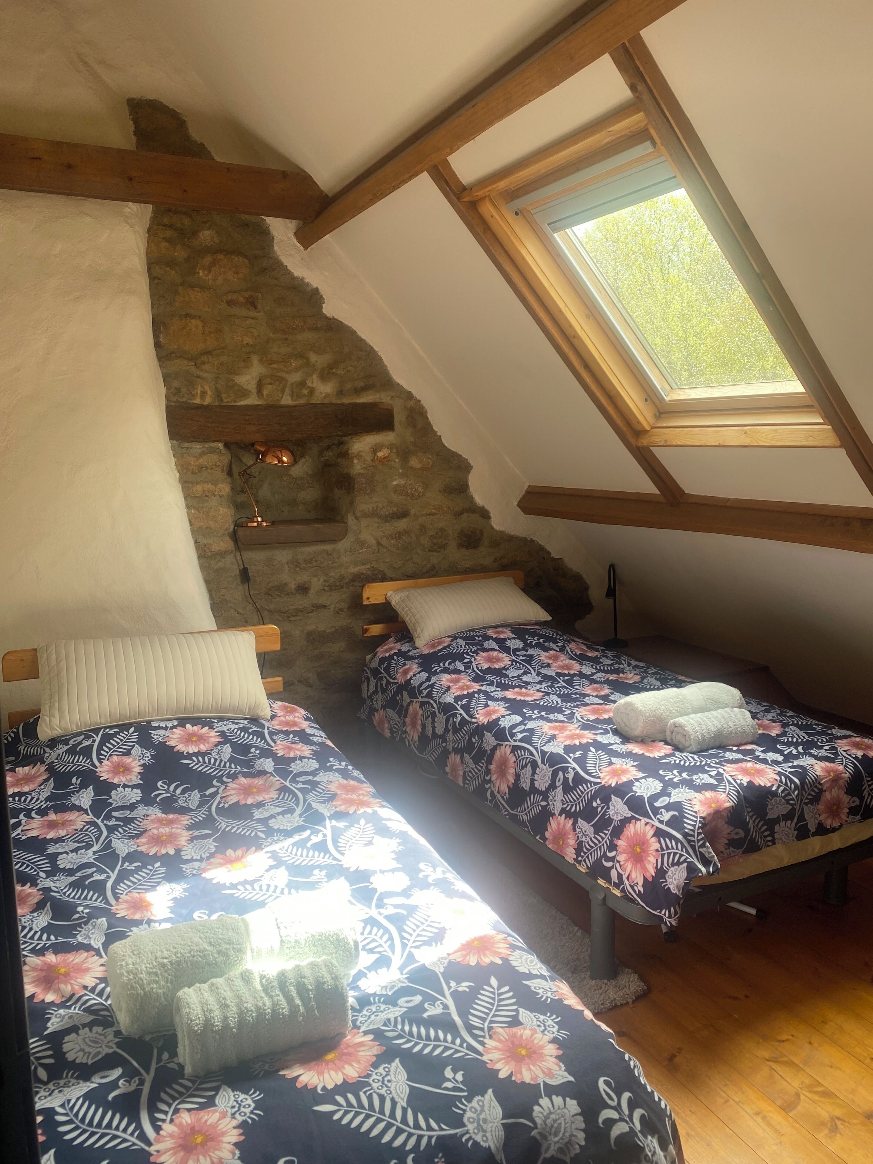 A room with two beds, a sloped ceiling, a skylight, and a stone wall.