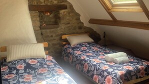 Ein Zimmer mit zwei Betten, einer schrägen Decke, einem Oberlicht und einer Steinwand.