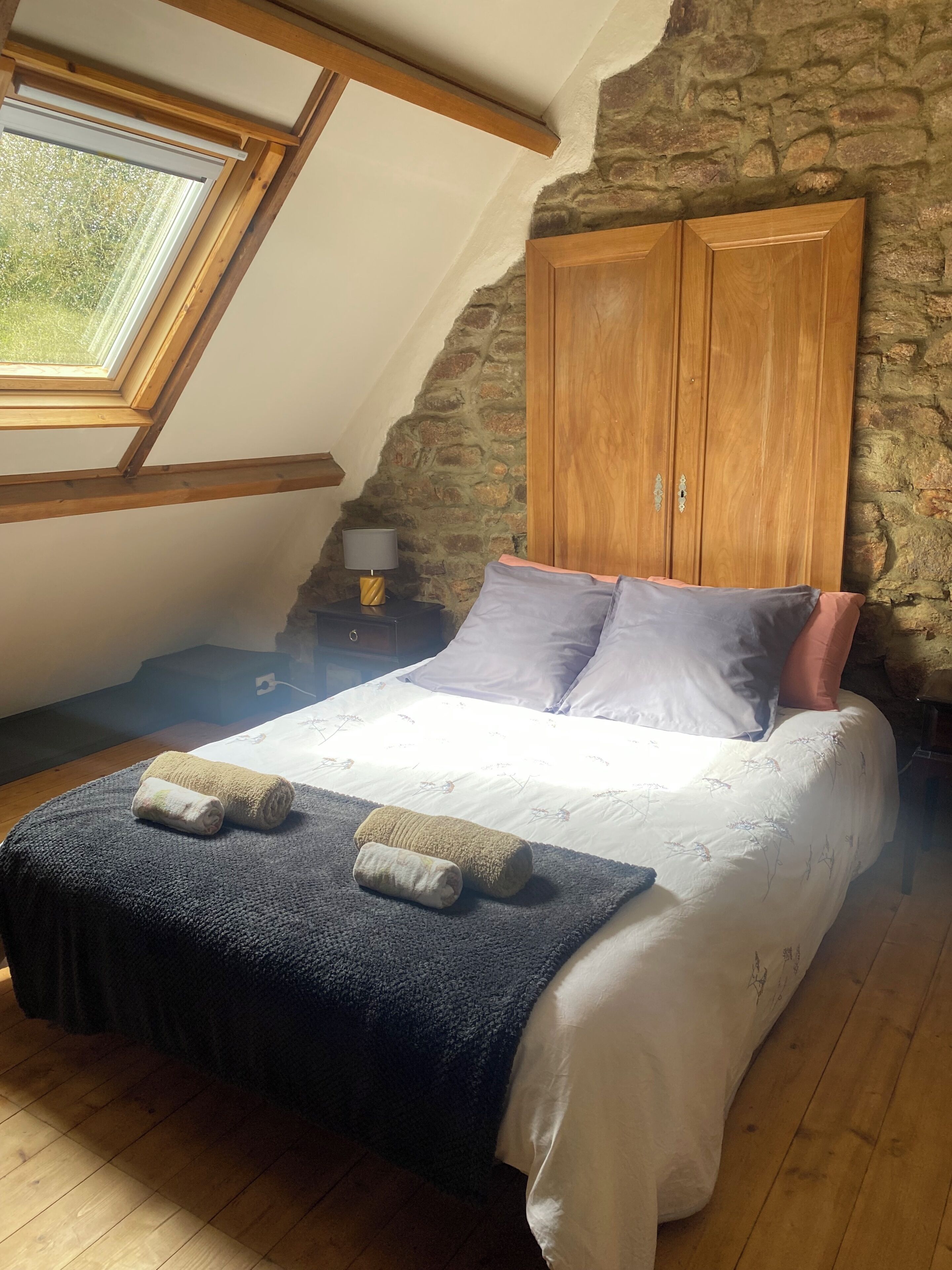 A bedroom with a sloped ceiling, a stone wall, and a wooden wardrobe.