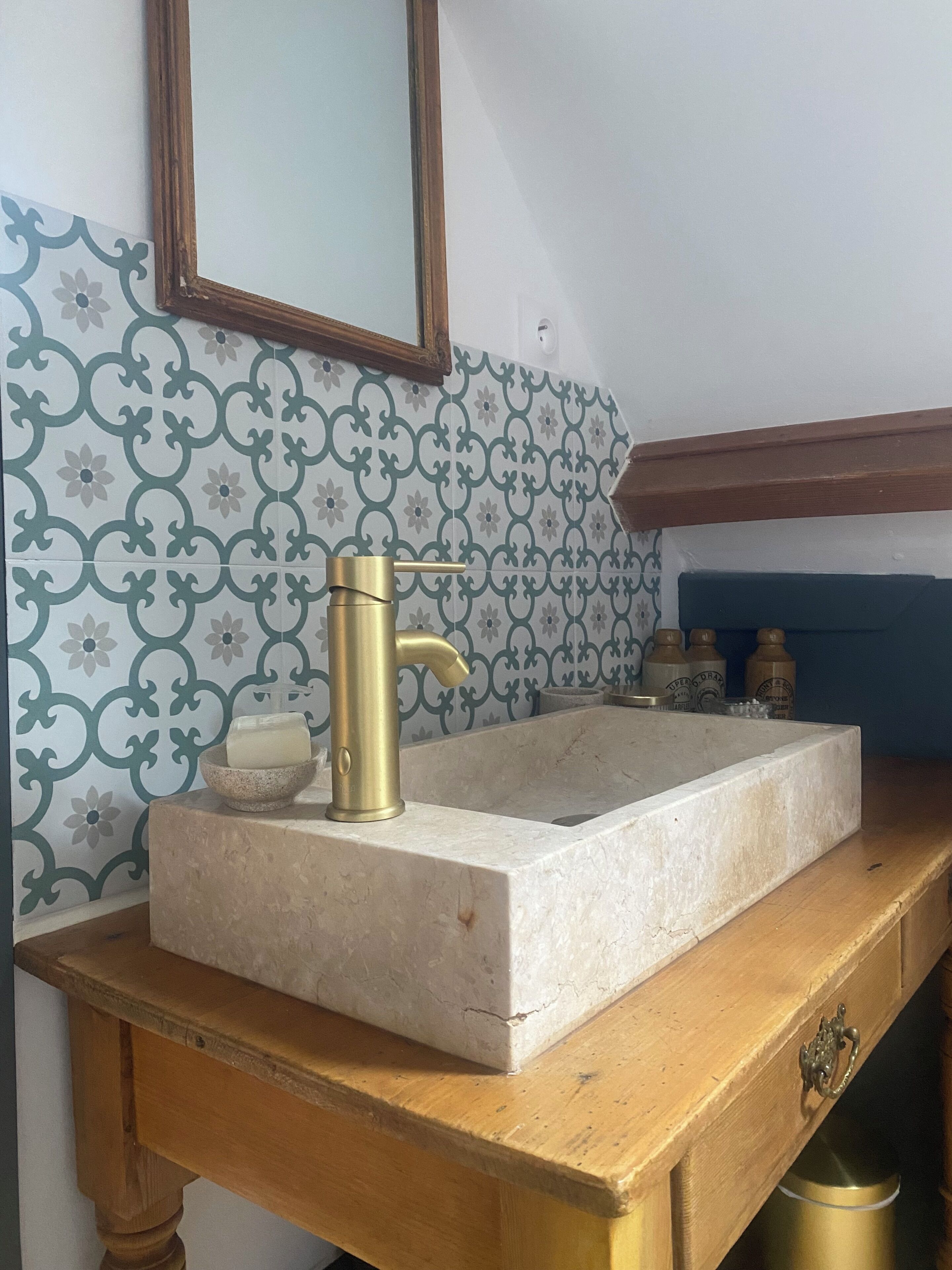 Une salle de bain avec un lavabo en marbre, un robinet doré et des carreaux muraux à motifs.