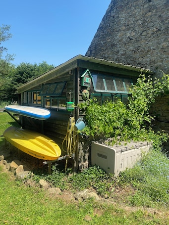 A rustic cabin with a small porch, a birdhouse, and a kayak.. Lost Er Lann - Charming gîte on the banks of the Blavet river