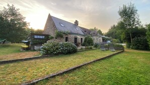 Ein Steinhäuschen mit einem geneigten Dach, ein kleiner Garten mit Hortensien und ein gepflasterter Weg zum Eingang.