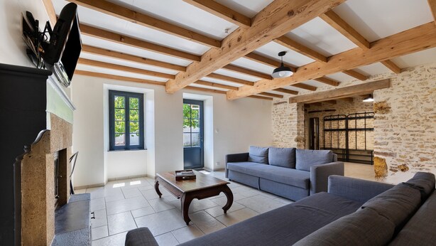 Una sala de estar con pared de piedra, vigas de madera, un sofá y una chimenea.