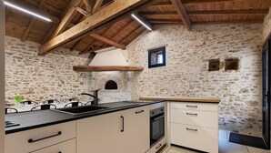 Una cocina con paredes de piedra, vigas de madera, horno empotrado y un lavabo.