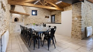 Comedor de paredes de piedra con una mesa larga y sillas, vigas de madera en el techo y una ventana pequeña.