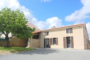 A two-story building with a beige facade, a red-tiled roof, and shuttered windows.