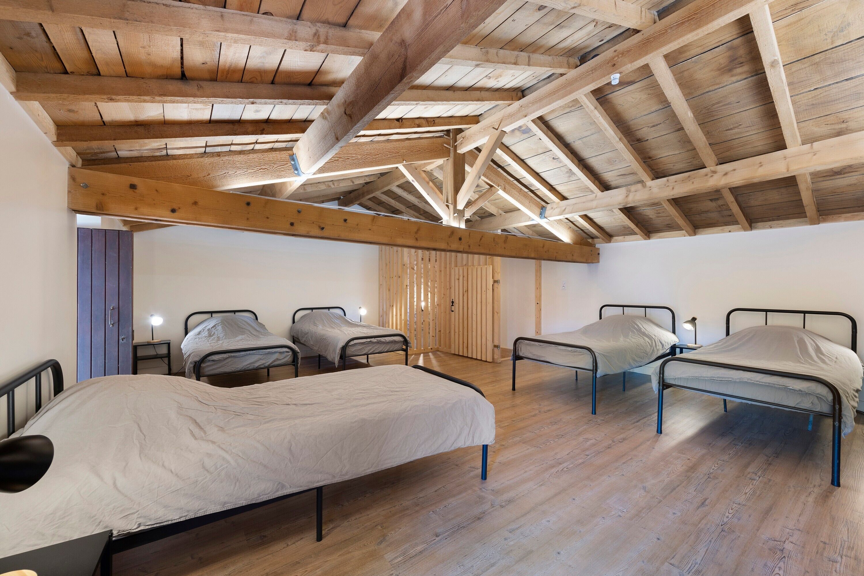 Une pièce avec quatre lits en métal, des poutres en bois au plafond et un plancher en bois.