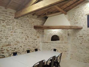 A stone-walled room with a white table and chairs, a wooden ceiling, and a stone fireplace.