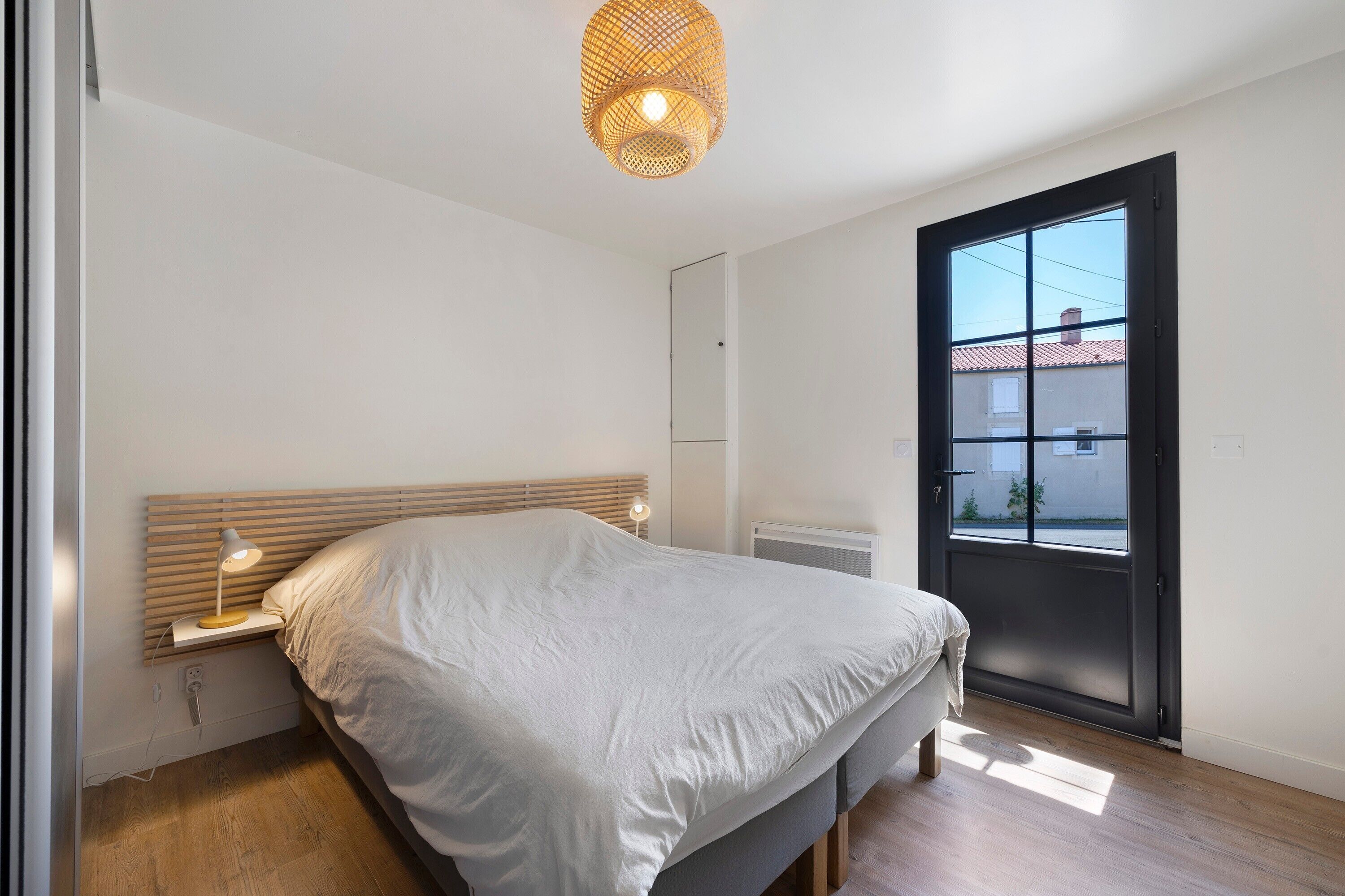 Een moderne slaapkamer met een groot bed, nachtlampjes, een plafondlamp en uitzicht door een deur.
