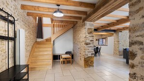Un interior espacioso con vigas de madera a la vista, una pared de piedra, una escalera y un comedor.