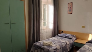 Habitació amb un llit, una panxa, un armari i una finestra amb cortines.