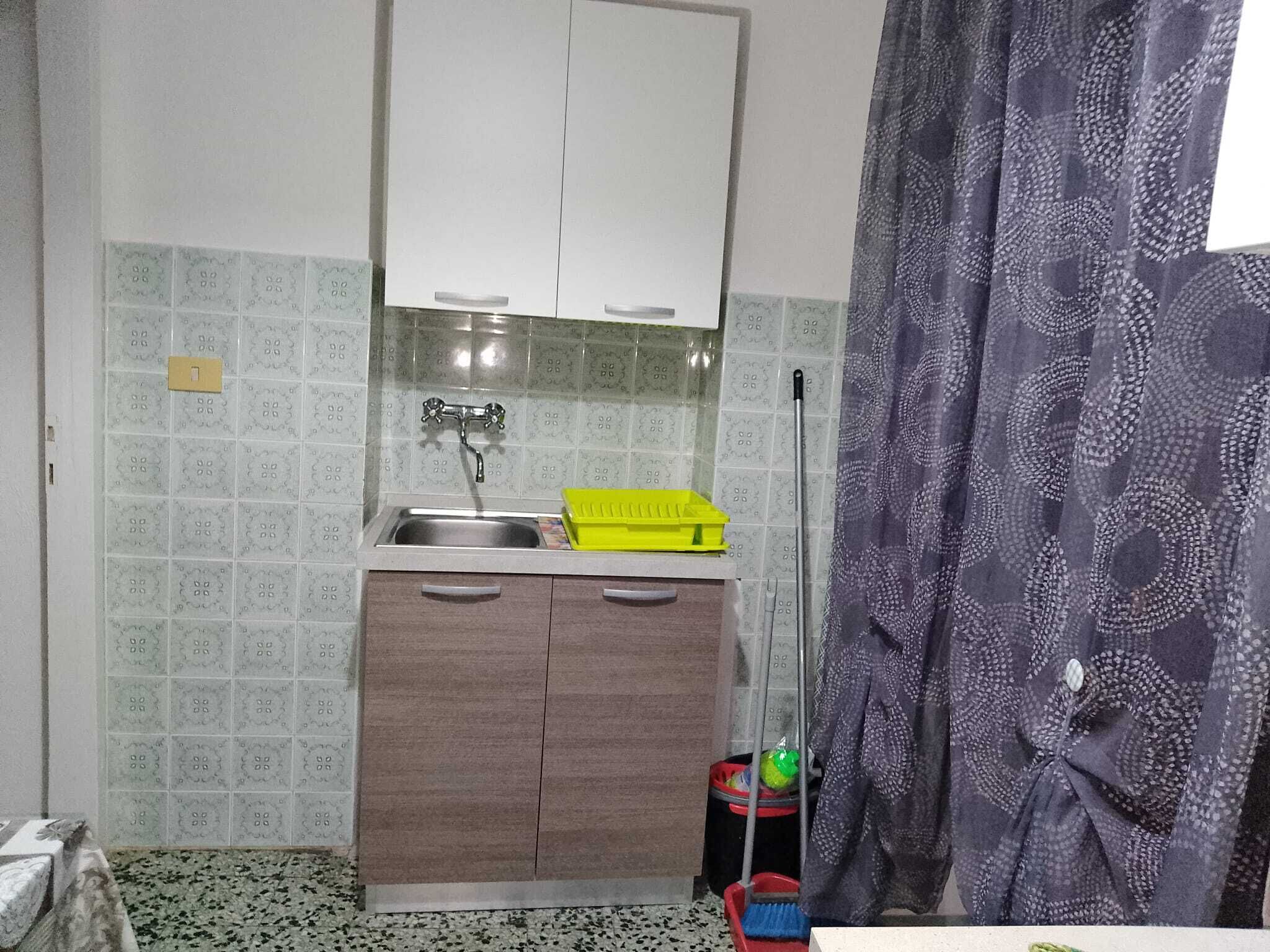 A small kitchenette with a sink, cabinets, and a broom.
