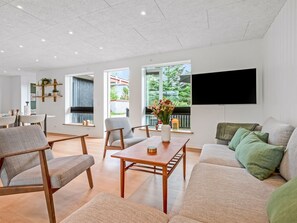 Ein modernes Wohnzimmer mit einer Couch, Sesseln, einem Couchtisch und einem Fernseher.