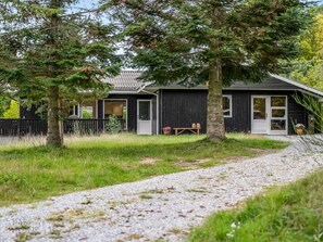 Ein Haus mit Kiesweg, Holzpforte und einem Baum im Vordergrund.