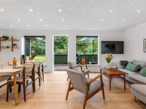 A spacious living area with a dining table, chairs, a sofa, and a TV mounted on the wall.